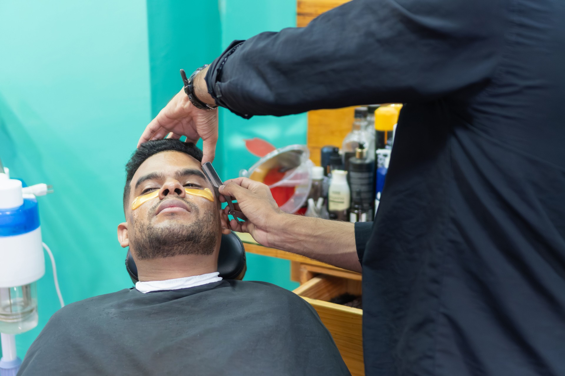 Hairdresser shaving client's beard in beauty salon with razor